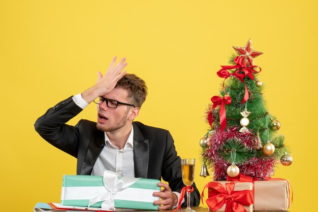 Vista frontal del trabajador masculino detrás de su lugar de trabajo con diferentes regalos en amarillo