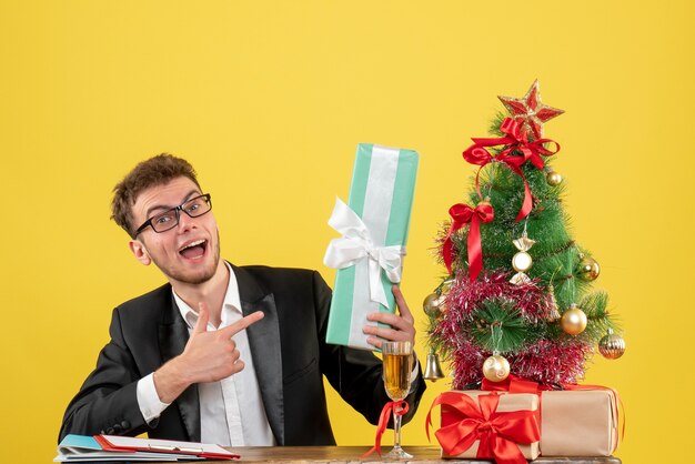 Vista frontal del trabajador masculino detrás de su lugar de trabajo con diferentes regalos en amarillo