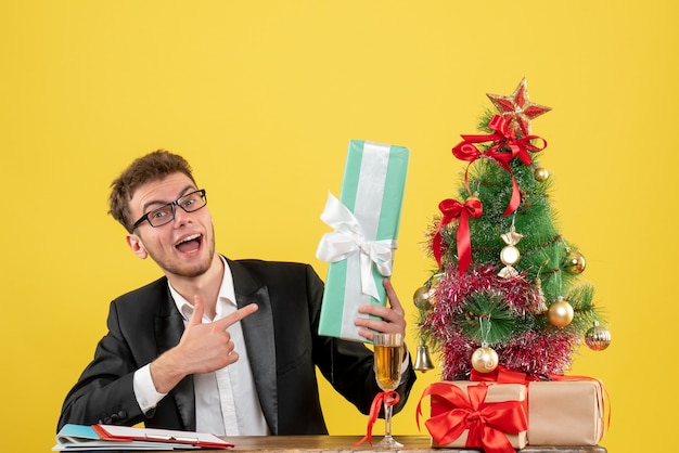 Vista frontal del trabajador masculino detrás de su lugar de trabajo con diferentes regalos en amarillo