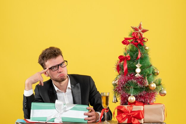 Vista frontal del trabajador masculino detrás de su lugar de trabajo con diferentes regalos en amarillo