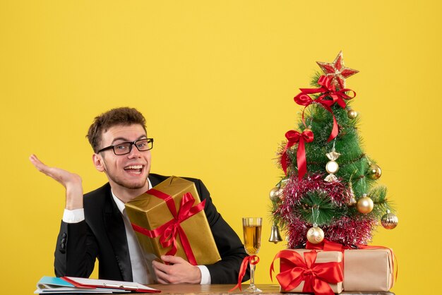 Vista frontal del trabajador masculino detrás de su lugar de trabajo con diferentes regalos en amarillo