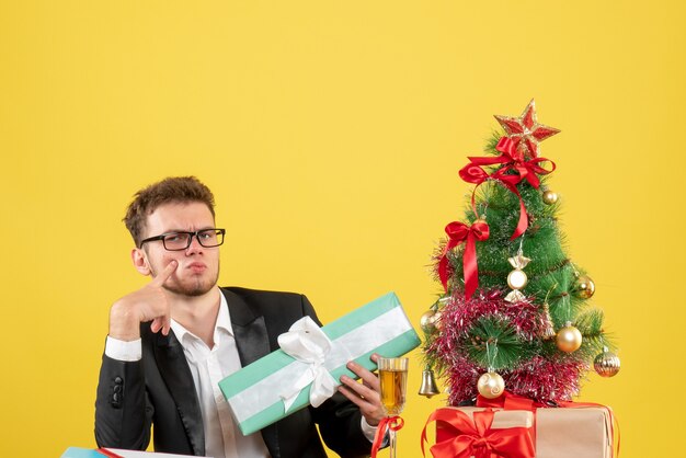 Vista frontal del trabajador masculino detrás de su lugar de trabajo con diferentes regalos en amarillo