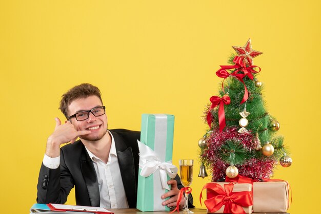 Vista frontal del trabajador masculino detrás de su lugar de trabajo con diferentes regalos en amarillo