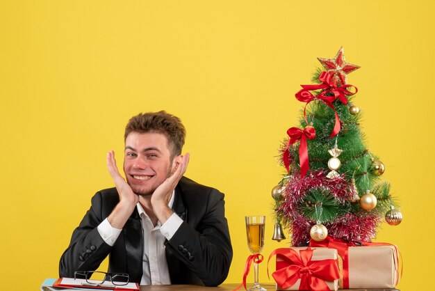 Vista frontal del trabajador masculino detrás de su lugar de trabajo con regalos en amarillo