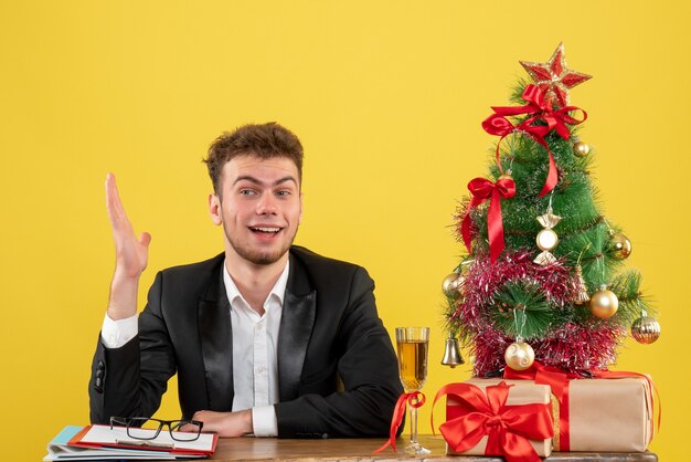 Vista frontal del trabajador masculino detrás de su lugar de trabajo con regalos en amarillo