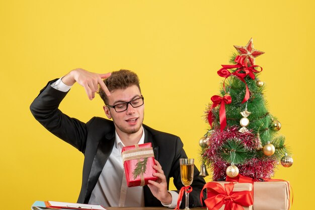 Vista frontal del trabajador masculino detrás de su lugar de trabajo con regalos en amarillo