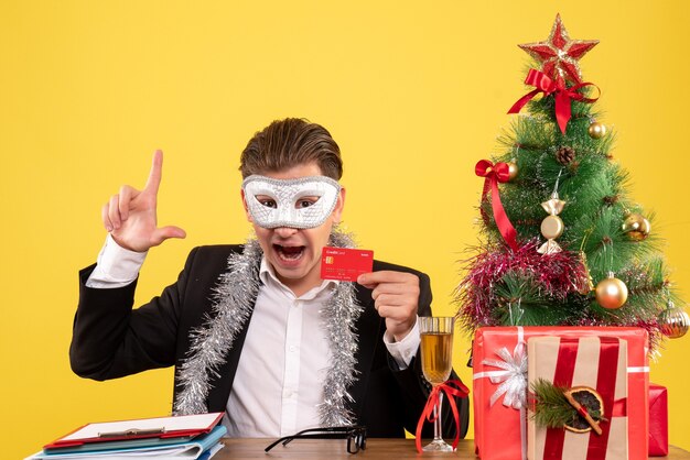 Vista frontal del trabajador masculino con máscara de fiesta y sosteniendo una tarjeta bancaria