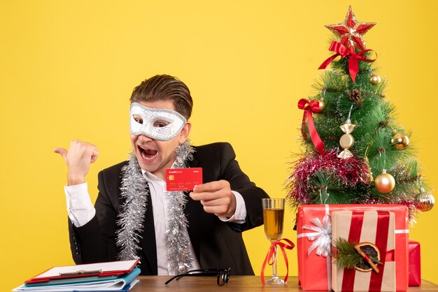 Vista frontal del trabajador masculino con máscara de fiesta y sosteniendo una tarjeta bancaria