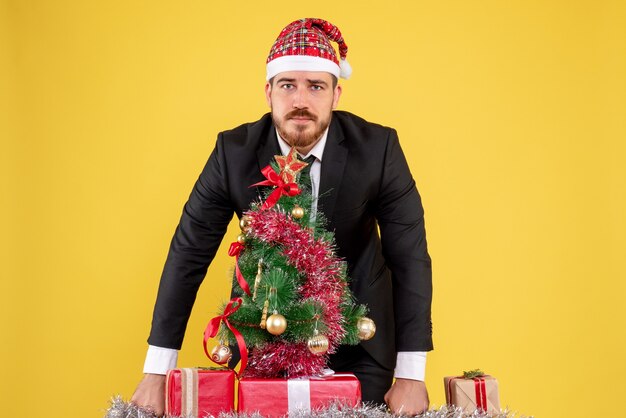 Vista frontal trabajador masculino de pie detrás de su lugar de trabajo con regalos en amarillo
