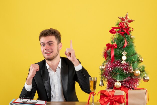 Vista frontal del trabajador masculino sentado detrás de su lugar de trabajo en amarillo