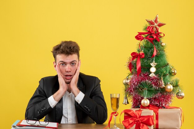 Vista frontal del trabajador masculino sentado detrás de su lugar de trabajo en amarillo