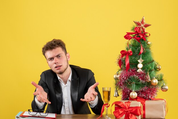 Vista frontal del trabajador masculino sentado detrás de su lugar de trabajo en amarillo