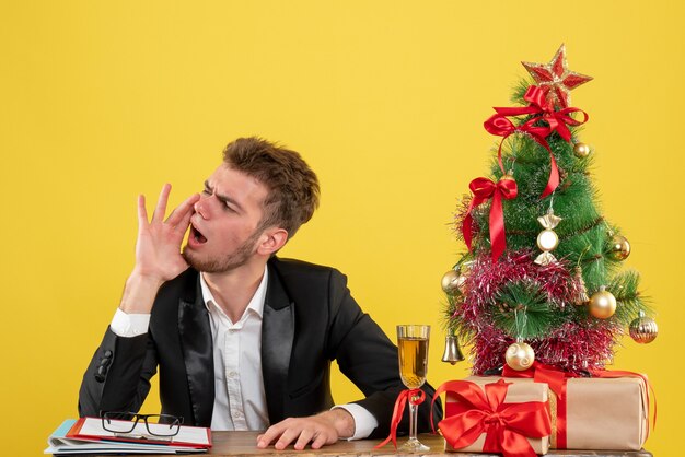 Vista frontal trabajador masculino sentado detrás de su lugar de trabajo pidiendo amarillo