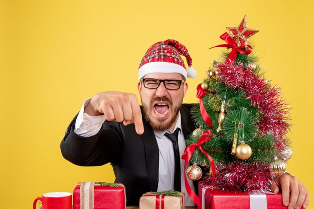 Vista frontal trabajador masculino sentado detrás de su lugar de trabajo con regalos en amarillo