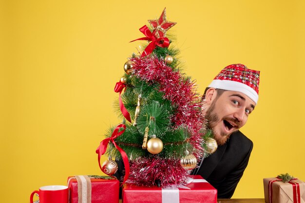 Vista frontal trabajador masculino sentado detrás de su lugar de trabajo con regalos en amarillo