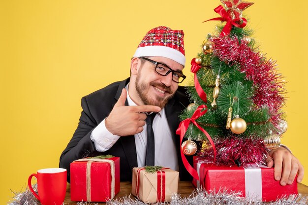 Vista frontal trabajador masculino sentado detrás de su lugar de trabajo con regalos en amarillo