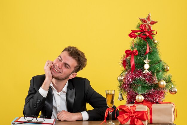 Vista frontal trabajador masculino sentado detrás de su lugar de trabajo sonriendo en amarillo