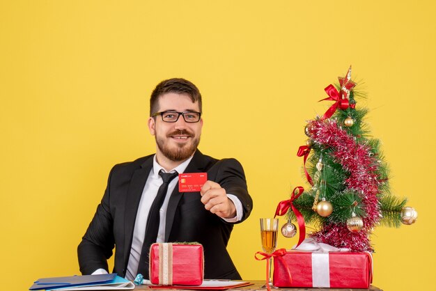 Vista frontal del trabajador masculino sentado detrás de su lugar de trabajo con tarjeta bancaria en amarillo