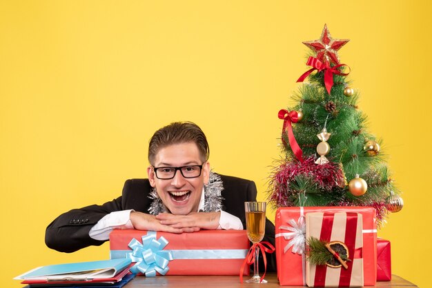 Vista frontal trabajador masculino sentado con regalos de Navidad