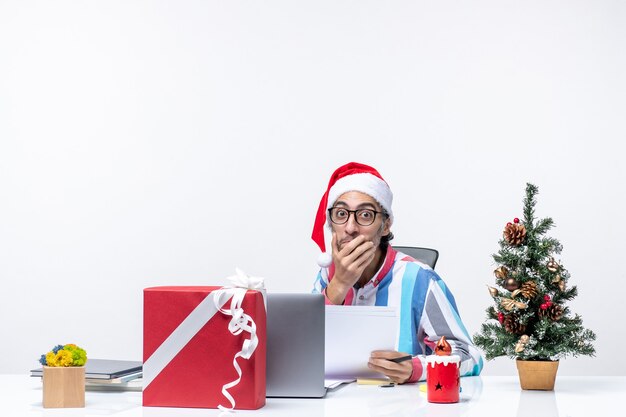 Vista frontal del trabajador masculino sentado en su lugar con una computadora portátil y archivos con documentos emociones de la oficina de Navidad
