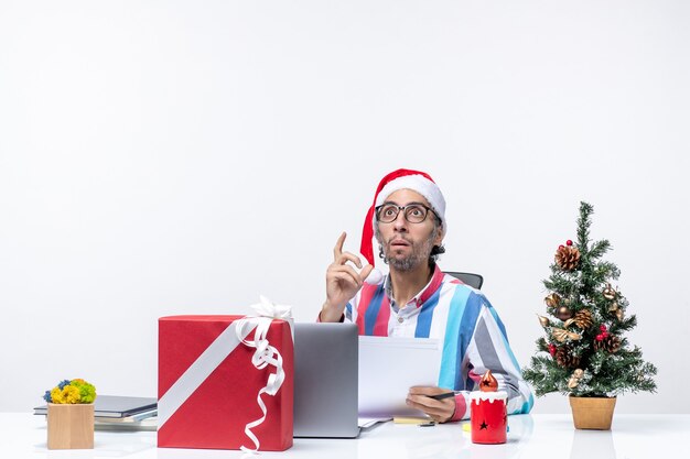 Vista frontal del trabajador masculino sentado en su lugar con una computadora portátil y archivos con documentos de oficina de Navidad