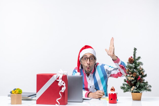 Vista frontal del trabajador masculino sentado en su lugar escribiendo notas y usando la emoción de la computadora portátil en la oficina de Navidad