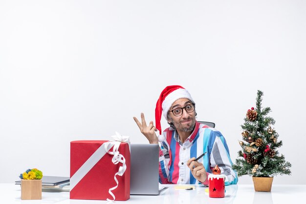 Vista frontal trabajador masculino sentado en su lugar con laptop y archivos posando emoción de Navidad de trabajo de oficina