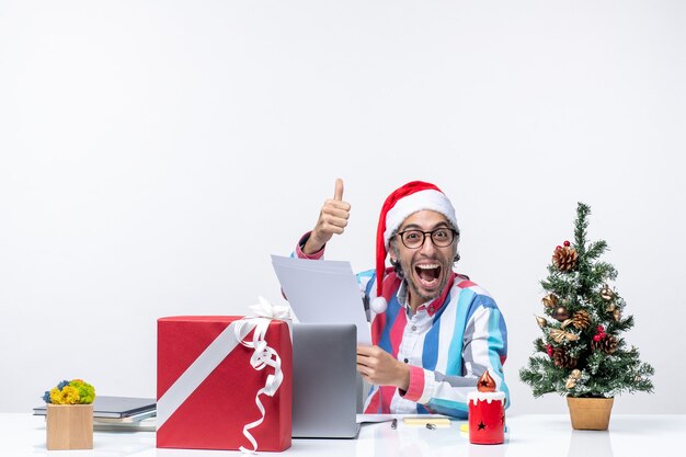 Vista frontal trabajador masculino sentado en su lugar con laptop leyendo documentos oficina trabajo emoción navidad