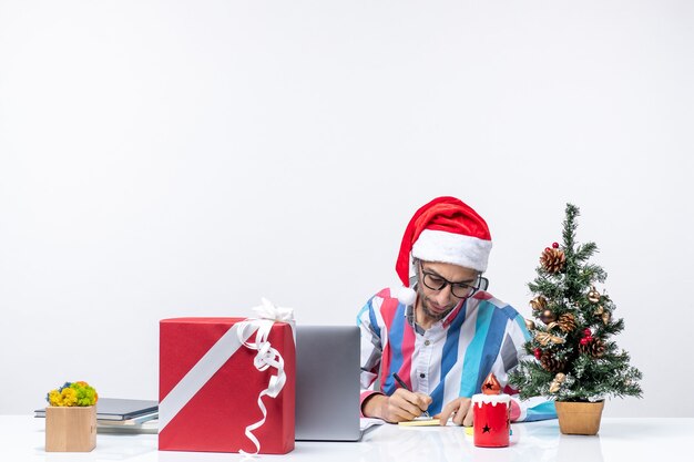 Vista frontal trabajador masculino sentado en su lugar con portátil y archivos escribiendo notas trabajo de oficina de vacaciones de Navidad