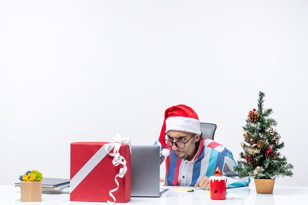 Vista frontal del trabajador masculino sentado en su lugar con el portátil y los archivos de trabajo de oficina de trabajo de vacaciones de Navidad