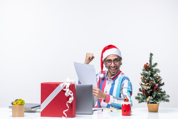 Vista frontal del trabajador masculino sentado en su lugar con el portátil leyendo documentos emoción trabajo de oficina navidad
