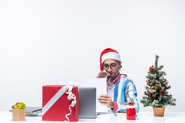 Vista frontal del trabajador masculino sentado en su lugar con un portátil sosteniendo documentos trabajo emoción oficina navidad