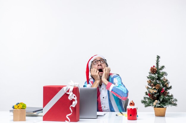 Vista frontal trabajador masculino sentado en su lugar de trabajo asustado de los cielos trabajo de emoción navideña de negocios