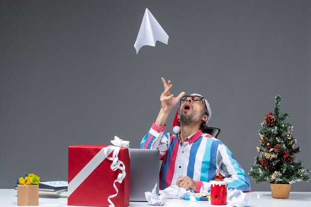 Vista frontal trabajador masculino sentado en su lugar de trabajo jugando con avión de papel