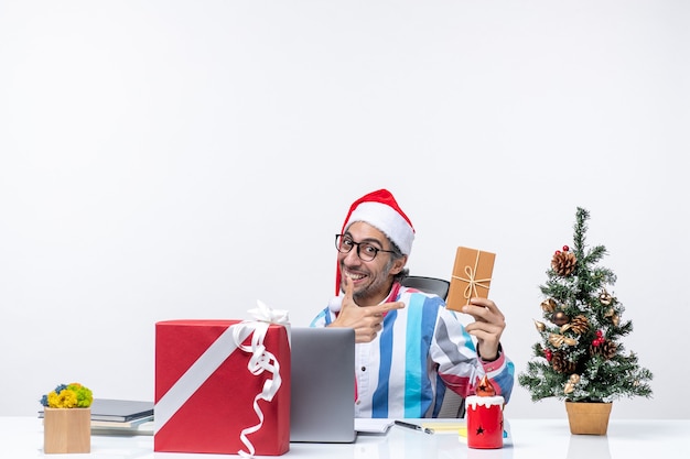 Foto gratuita vista frontal del trabajador masculino sentado en su lugar de trabajo con paquete de vacaciones emoción trabajo negocio de navidad