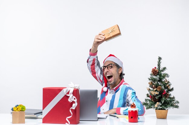Vista frontal trabajador masculino sentado en su lugar de trabajo con paquete vacaciones emociones trabajo de oficina de navidad