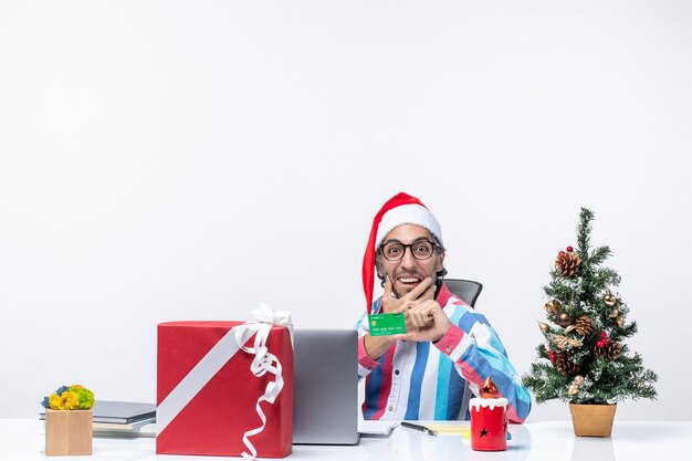 Vista frontal trabajador masculino sentado en su lugar de trabajo con tarjeta bancaria verde trabajo emoción navidad oficina dinero