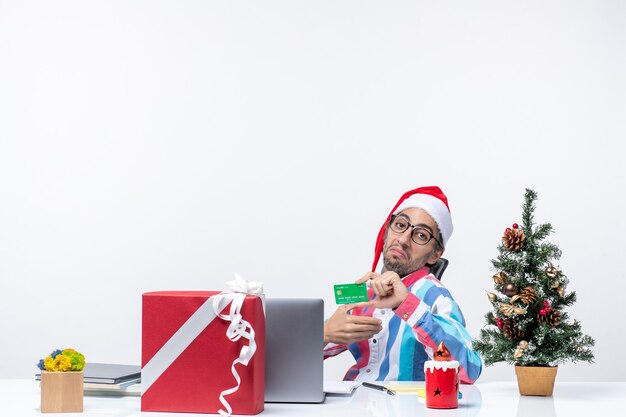 Vista frontal trabajador masculino sentado en su lugar de trabajo con tarjeta bancaria verde trabajo emoción oficina de navidad trabajo de dinero