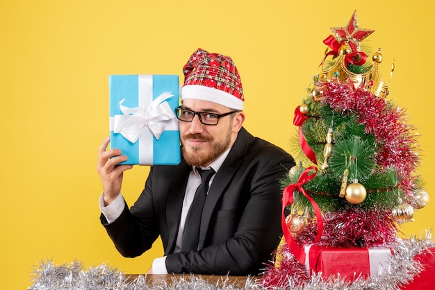 Vista frontal trabajador masculino sentados alrededor de regalos de Navidad en amarillo