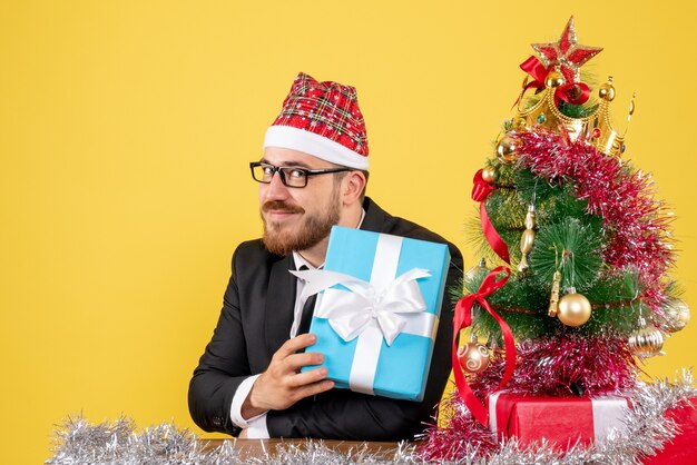 Vista frontal trabajador masculino sentados alrededor de regalos de Navidad en amarillo