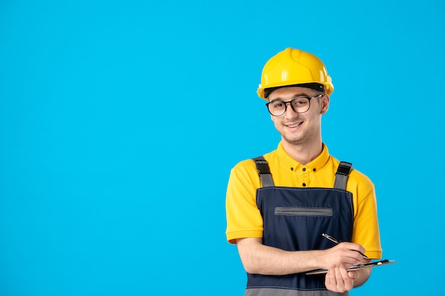 Vista frontal trabajador masculino en uniforme amarillo tomando notas sobre azul