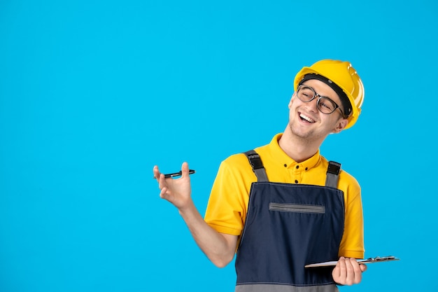 Vista frontal trabajador masculino en uniforme y casco tomando notas y riendo en azul