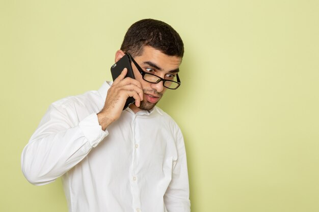 Vista frontal del trabajador de oficina masculino en camisa blanca hablando por teléfono en la pared verde claro