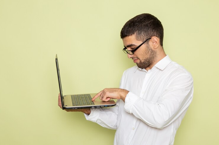 Foto gratuito vista frontal del trabajador de oficina masculino en camisa blanca con laptop en pared verde claro
