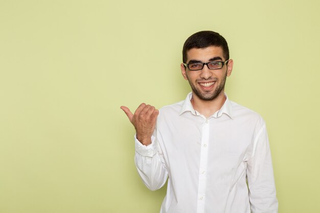 Vista frontal del trabajador de oficina masculino en camisa blanca sonriendo en la pared verde claro