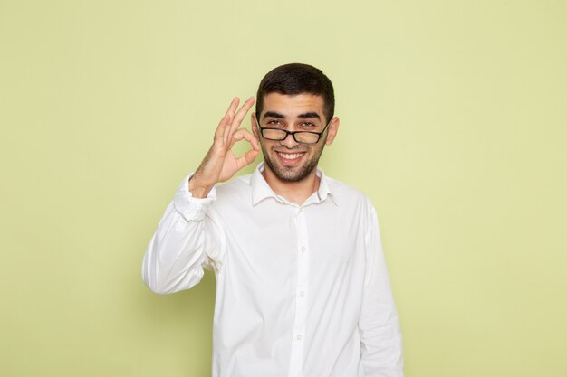 Vista frontal del trabajador de oficina masculino en camisa blanca sonriendo y posando en el escritorio verde claro trabajador de negocios trabajo de oficina trabajo masculino