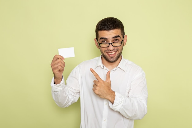 Foto gratuita vista frontal del trabajador de oficina masculino en camisa blanca con tarjeta de plástico blanco en la pared verde claro