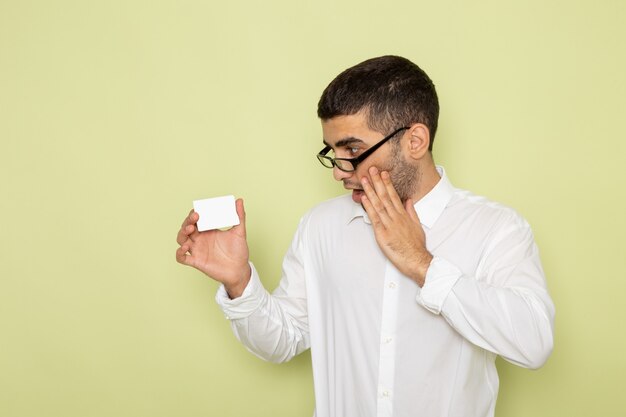 Vista frontal del trabajador de oficina masculino en camisa blanca con tarjeta de plástico en la pared verde claro