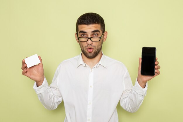 Vista frontal del trabajador de oficina masculino en camisa blanca con teléfono y tarjeta en la pared verde