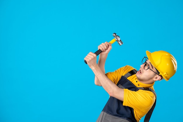 Vista frontal del trabajador de sexo masculino en uniforme amarillo con un martillo sobre un azul